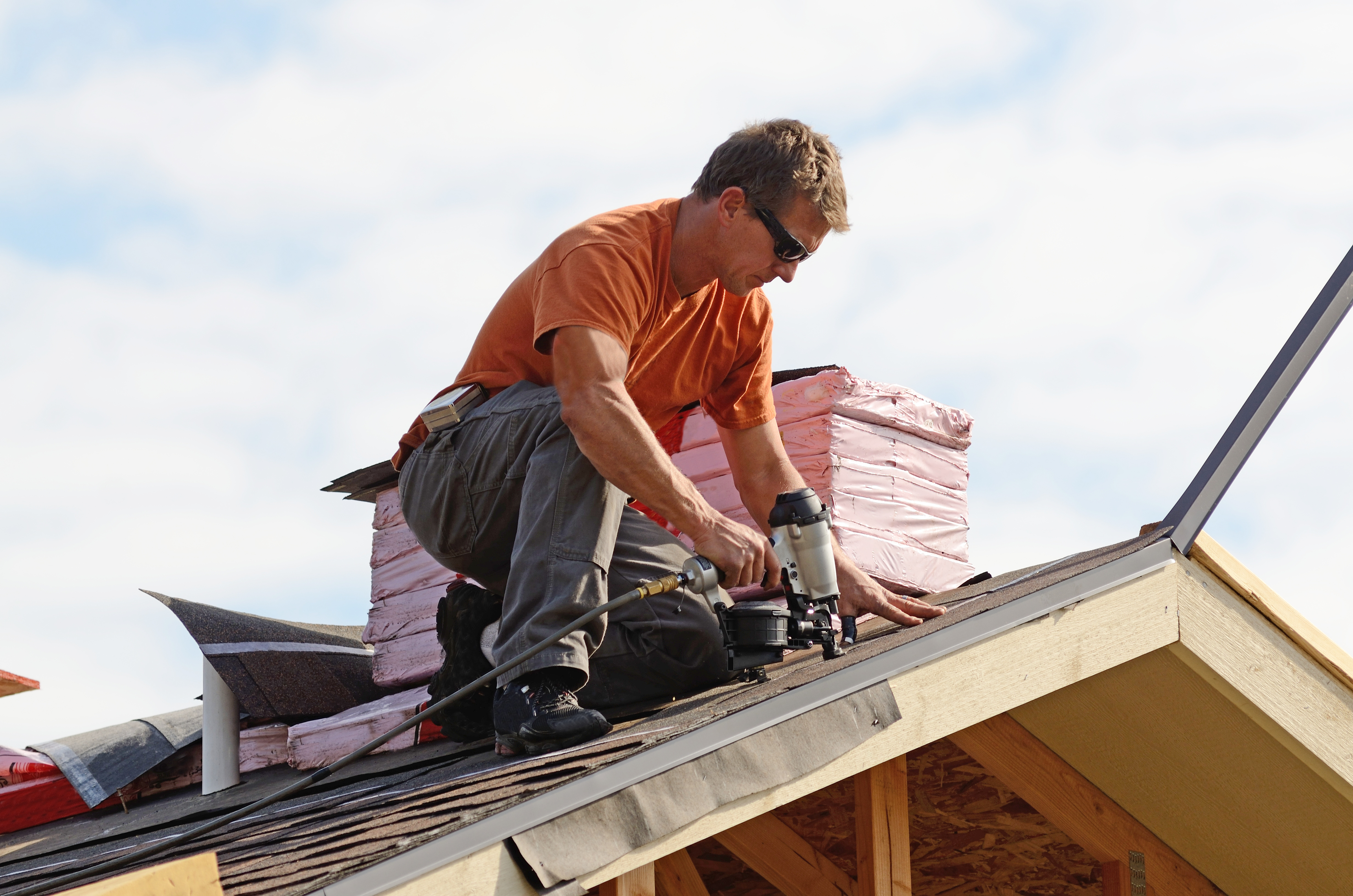 Roofer fastening shingles with a nail gun
