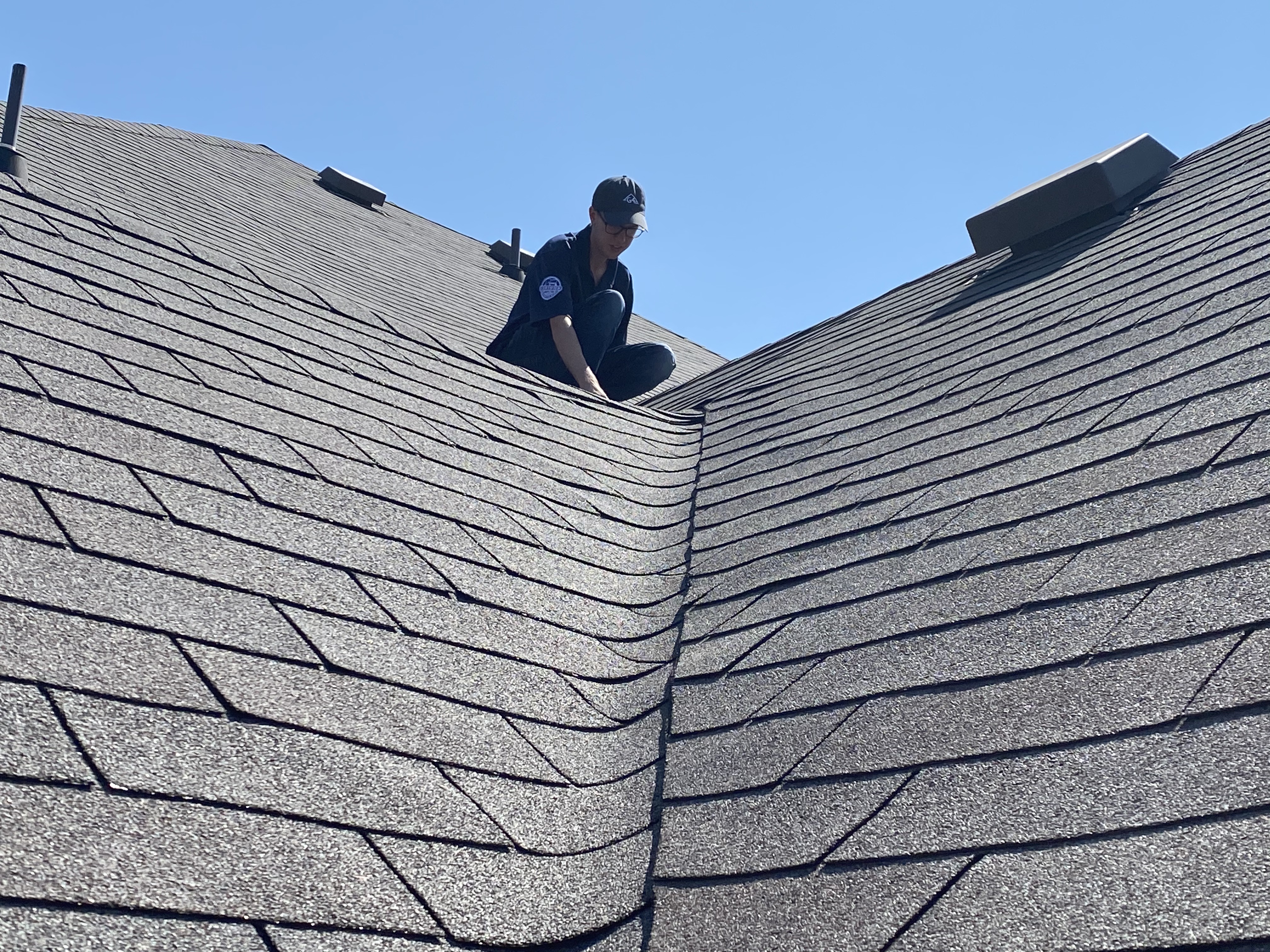 Roofer inspecting a shingle roof valley for damage